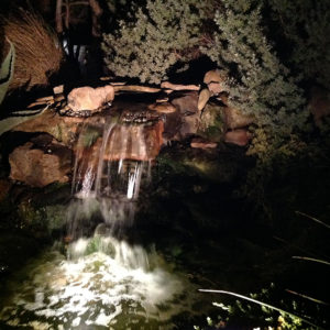 A backyard waterfall illuminated at night.