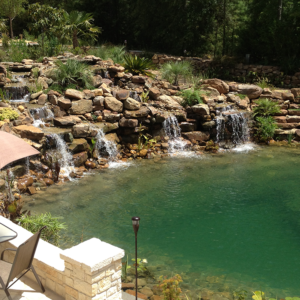 A wide waterfall with multiple streams of water pouring down into a large backyard pond.