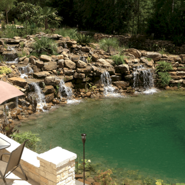 A wide waterfall with multiple streams of water pouring down into a large backyard pond.
