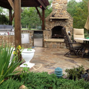 An expertly-crafted external stone fireplace next to a covered grill area and outdoor lounge.
