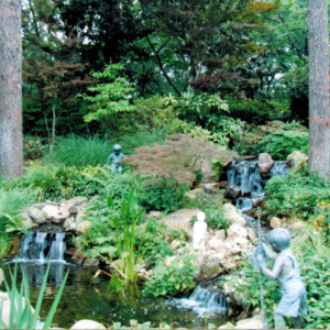A serene waterfall surrounded by trees, shrubbery, and statues in a freshly landscaped back yard.