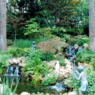 A serene waterfall surrounded by trees, shrubbery, and statues in a freshly landscaped back yard.