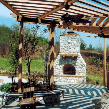 An expertly-crafted external stone fireplace next to a covered patio and swimming pool.