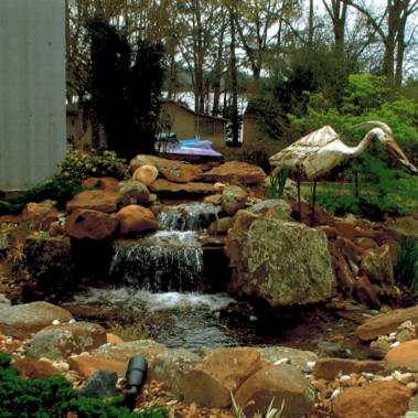 A multi-layer backyard waterfall with a metal bird statue on the side.