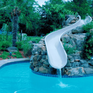 A winding slide perched on a stone structure leading to a pool in a back yard.