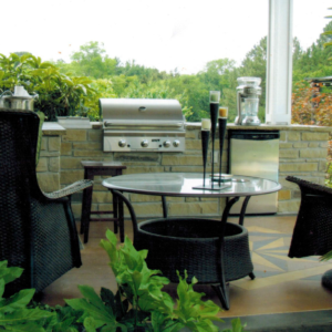 A modern backyard porch with sleek chairs and a table next to a grill mounted in a stone bar.