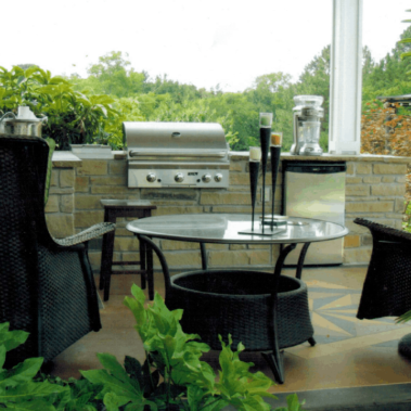 A modern backyard porch with sleek chairs and a table next to a grill mounted in a stone bar.