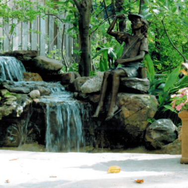 A bronze statue perched on a rock next to a backyard waterfall.