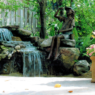 A bronze statue perched on a rock next to a backyard waterfall.