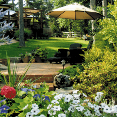 A backyard with an intricate landscape, including a variety of plants and large stone relaxation area covered by an umbrella.