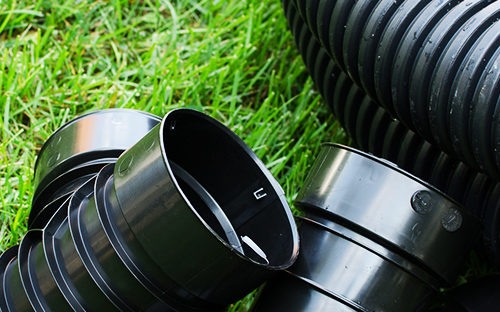 A close up of flexible drainage piping on a bright green lawn.