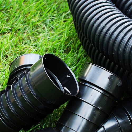 A close up of flexible drainage piping on a bright green lawn.