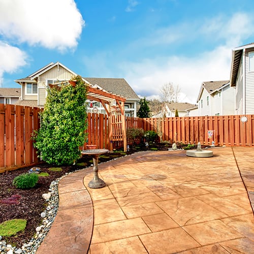 Beautiful tilework for a backyard area under a bright blue sky, with a brown wooden fence surrounding.
