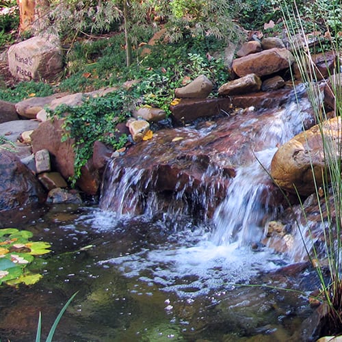 A wide waterfall with rushing water in a well-maintained backyard.