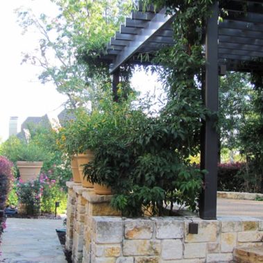 A freshly-landscaped backyard featuring stone walls and a wooden shade structure.