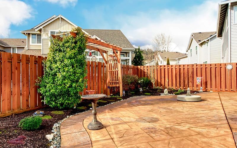 Beautiful tilework for a backyard area under a bright blue sky, with a brown wooden fence surrounding.